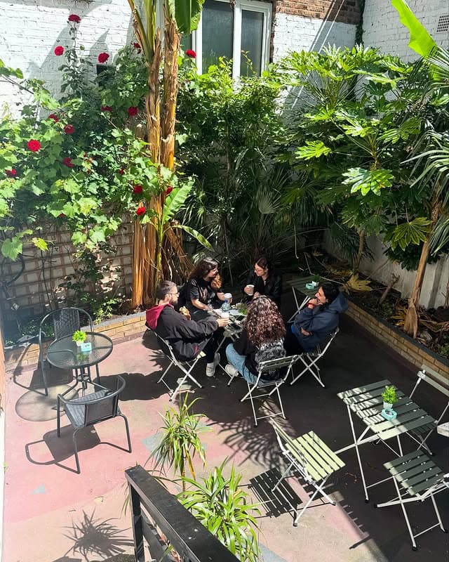 The back patio at Phyllo & Filo — sage bistro chairs, red roses and people seated among the greenery